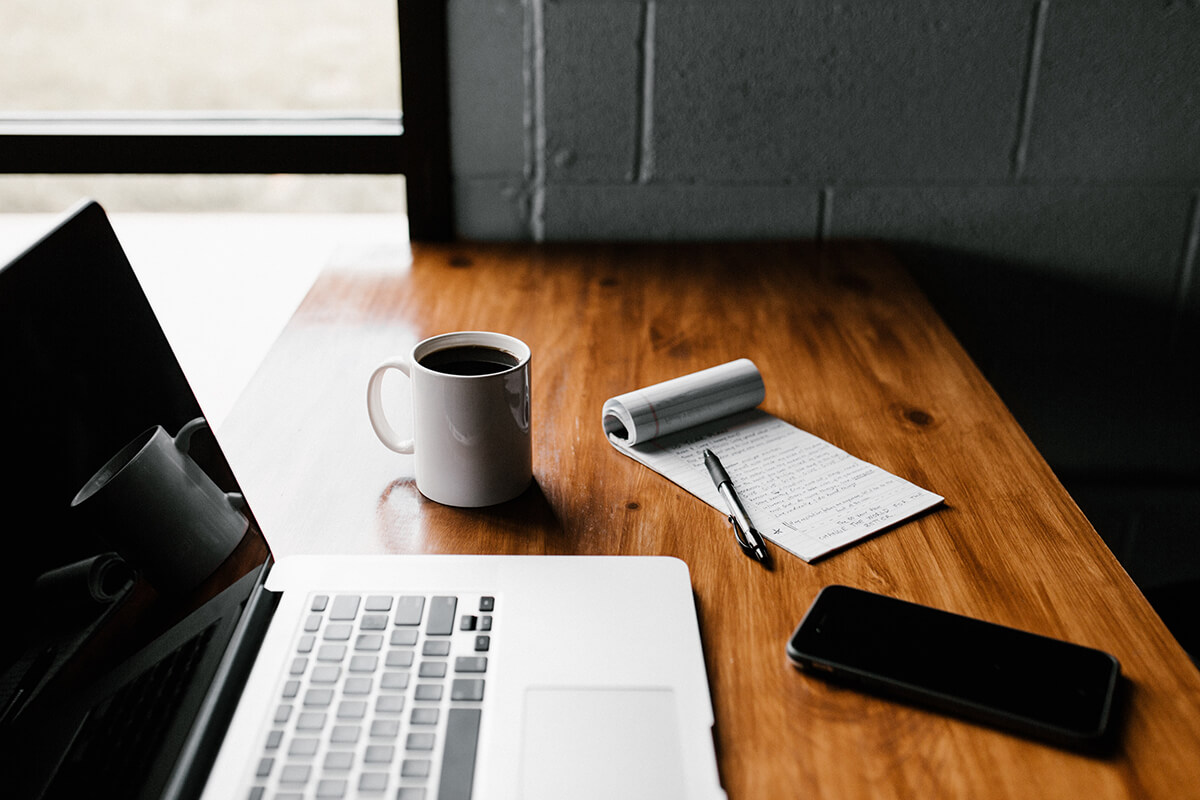 A table with laptop, pen, notebook, mobile and coffee